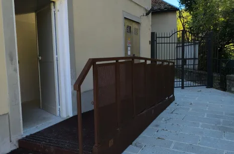 Rampa disabili in acciaio verniciato simil corten con pavimento in lamiera stirata antiscivolo e balaustra con pannelli in lamiera forata